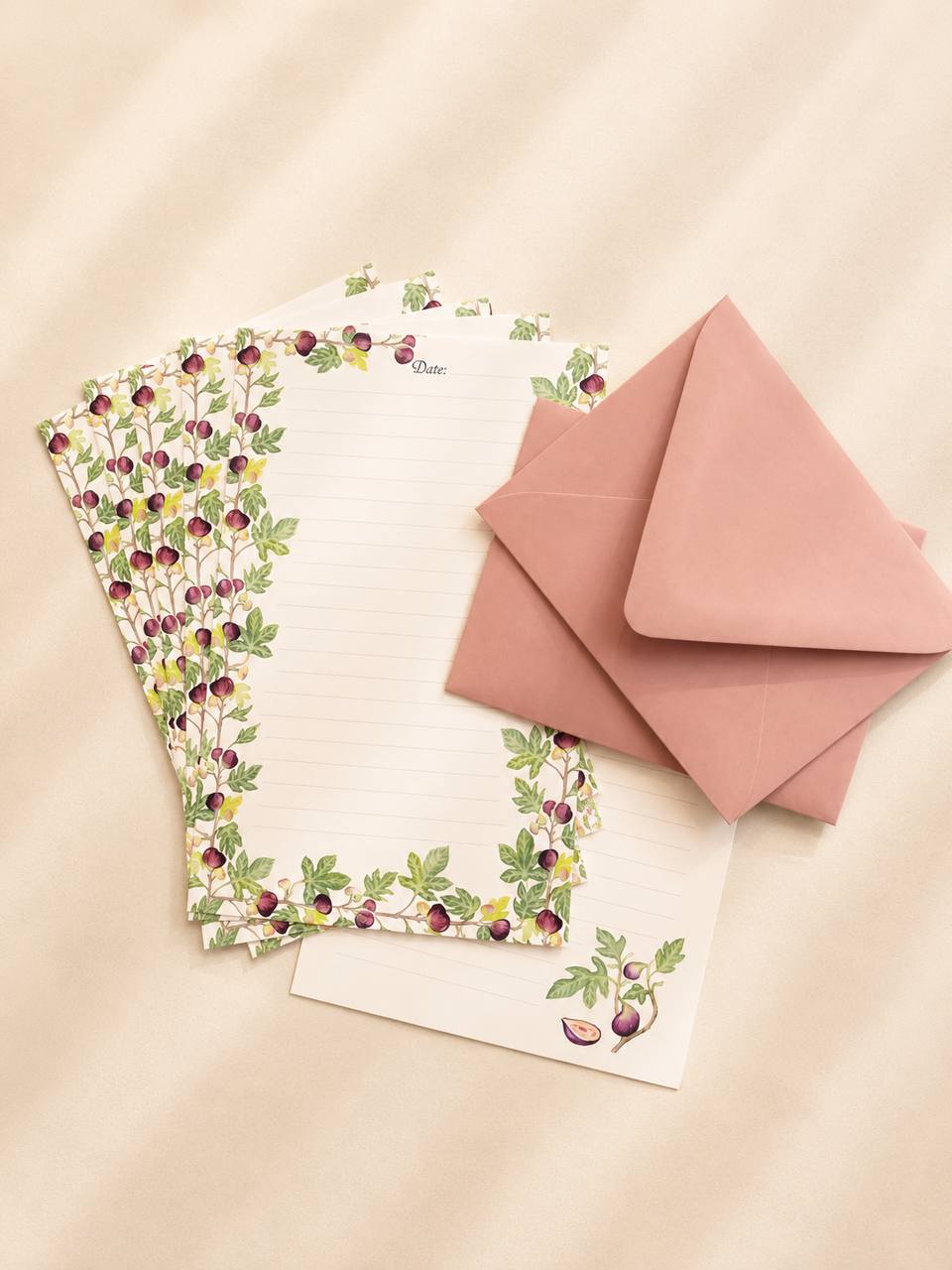 A fan of fig-patterned writing sheets beside two dusty-pink envelopes