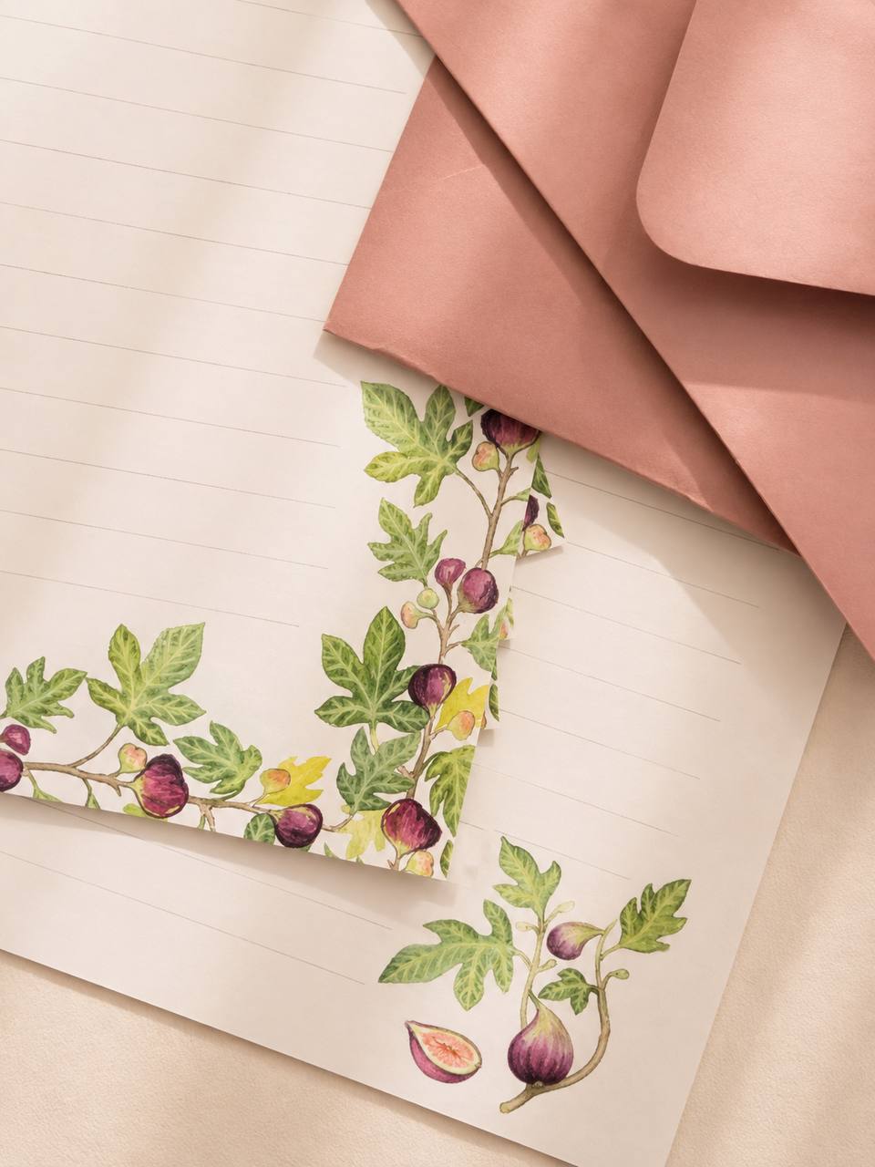 Fig-patterned writing paper with trailing leaves, laid over dusty-pink envelopes