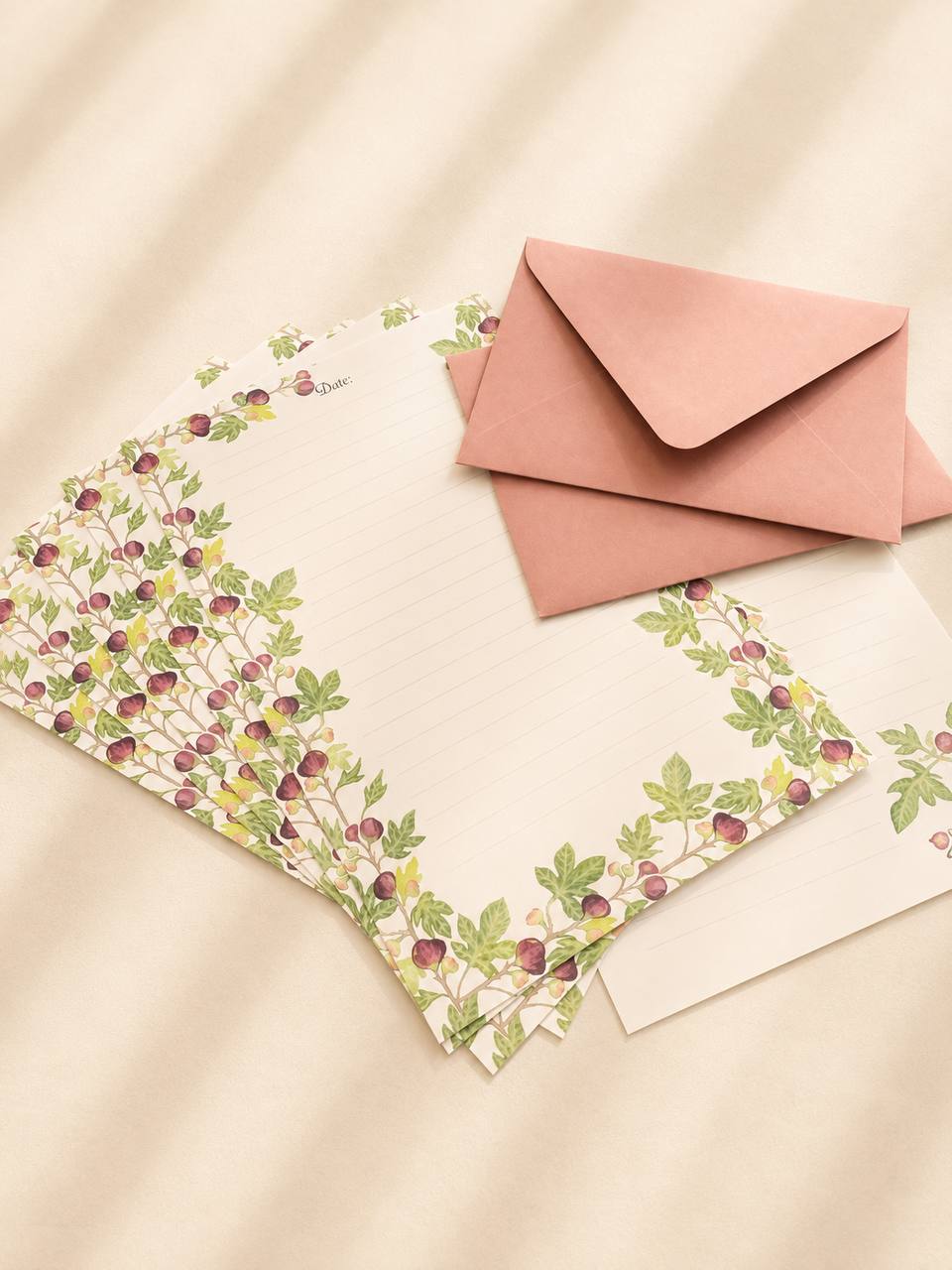 A fan of fig-patterned writing sheets beside a dusty-pink envelope