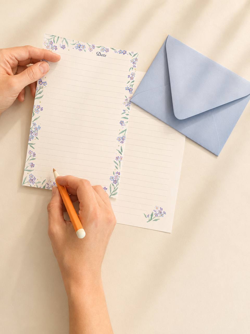 Forget-me-not writing paper and a powder-blue envelope, with a hand beginning a letter in pencil