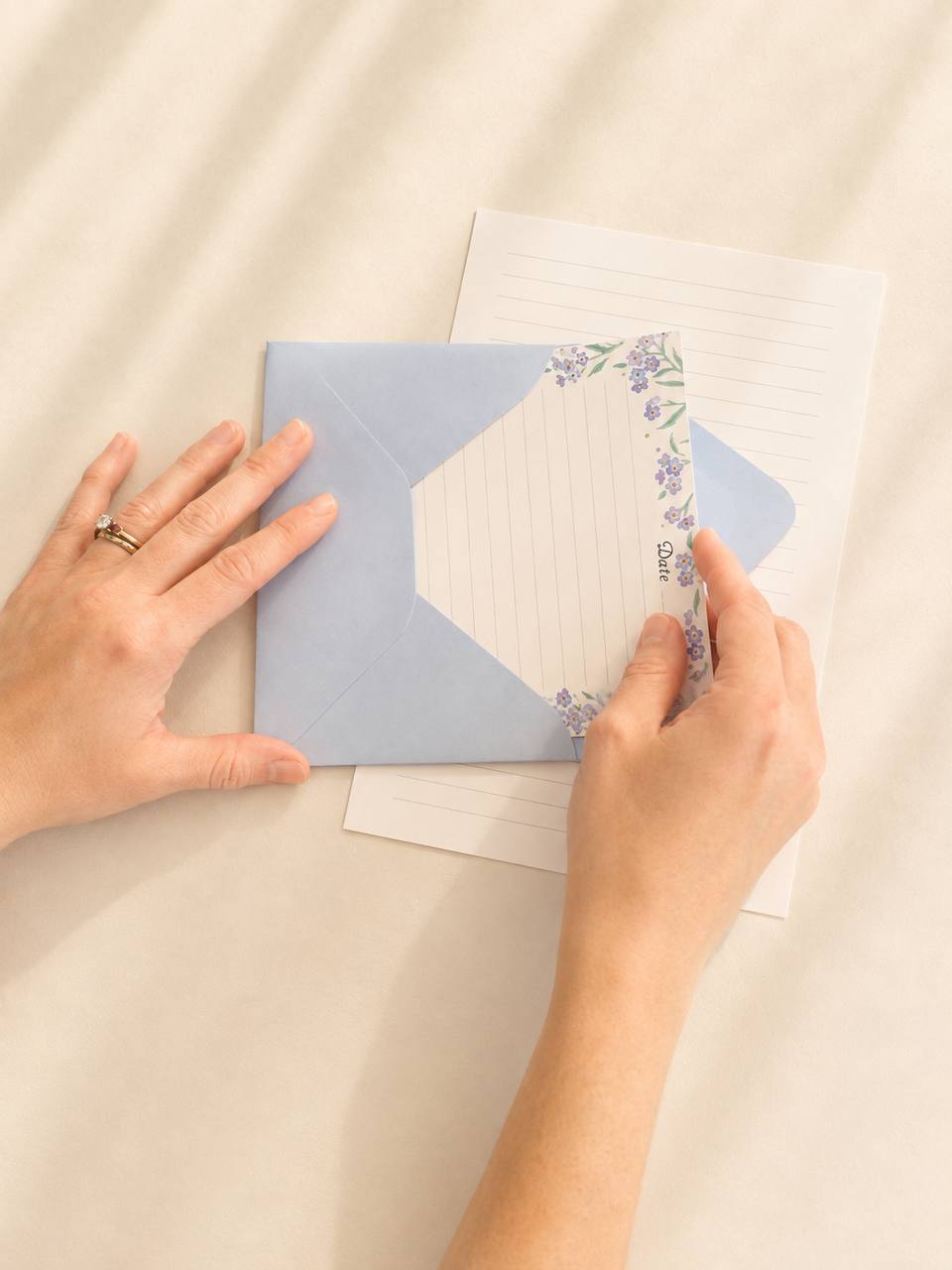 Hands tucking a forget-me-not letter into a powder-blue envelope