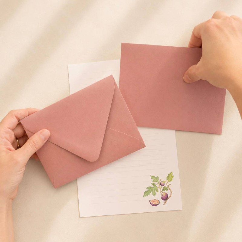 Hands holding a dusty-pink envelope above fig-patterned writing paper