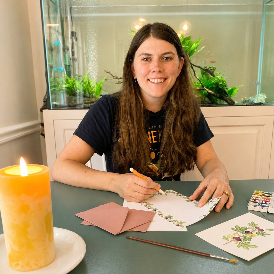 Hannah Lawson painting stationery at her table, a candle lit beside her