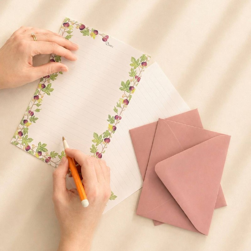 A hand writing on fig-patterned paper, dusty-pink envelopes alongside