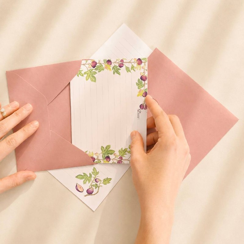 A fig-patterned letter being slid into a dusty-pink envelope