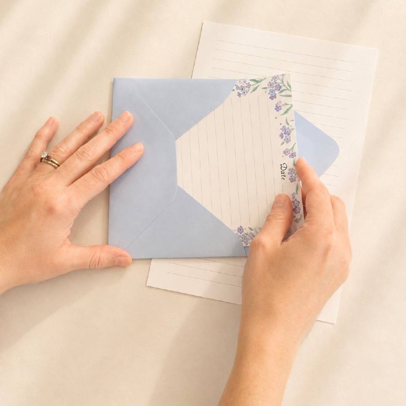 A forget-me-not letter being tucked into a powder-blue envelope