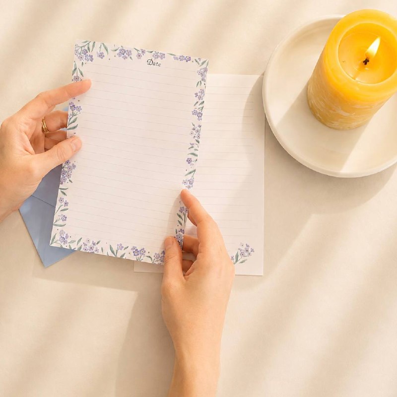 Hands smoothing a forget-me-not sheet beside a lit candle