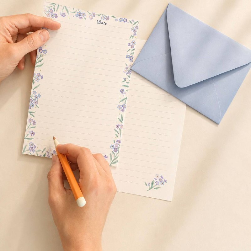 A hand writing on forget-me-not paper, a powder-blue envelope alongside